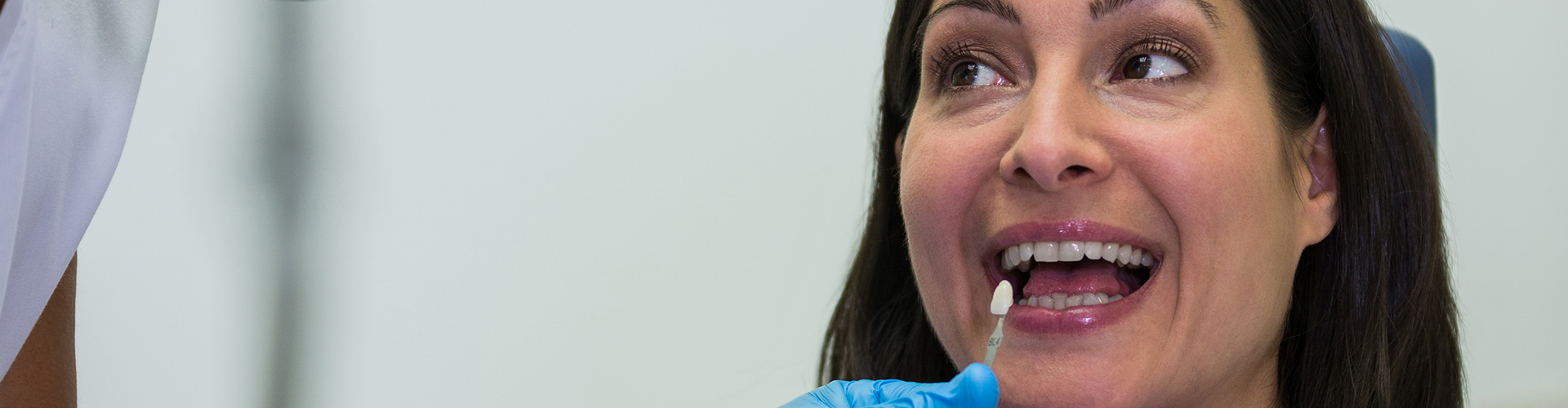 gloved hand holding tooth shade-matching tool against woman's teeth